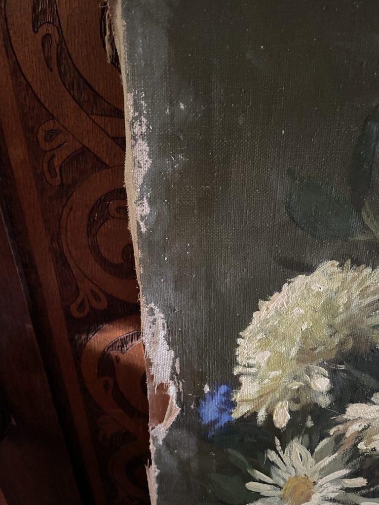 Close-up view of the edge of a floral painting with visible wear and texture.