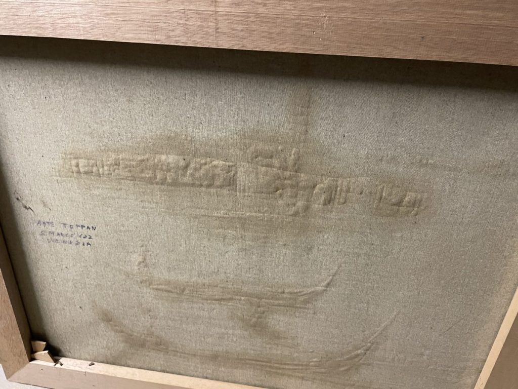 The back of a framed artwork showing a textured surface with markings and a wooden frame.