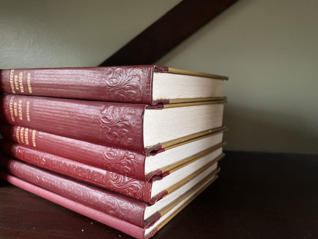 A stack of red-bound books with gold lettering on the spine, placed on a wooden surface.