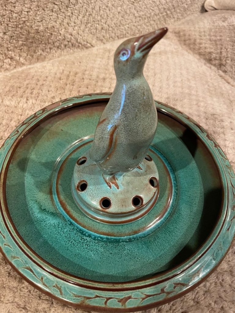 Ceramic penguin figurine on a circular base with multiple holes and decorative edges.