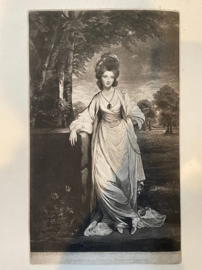 A woman in classical attire with a necklace, posed beside a stone structure in a landscape setting.