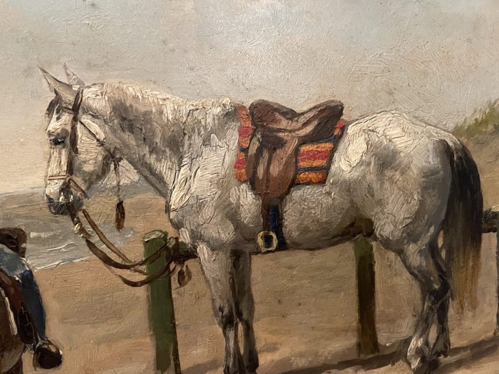 A gray horse standing beside a post with a saddle and bridle attached.
