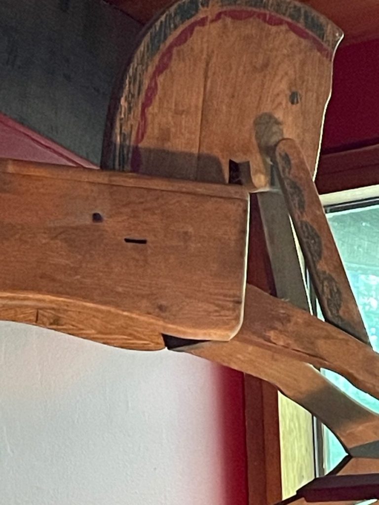 A vintage wooden rocking horse with a painted mane and tail, positioned against a wall.