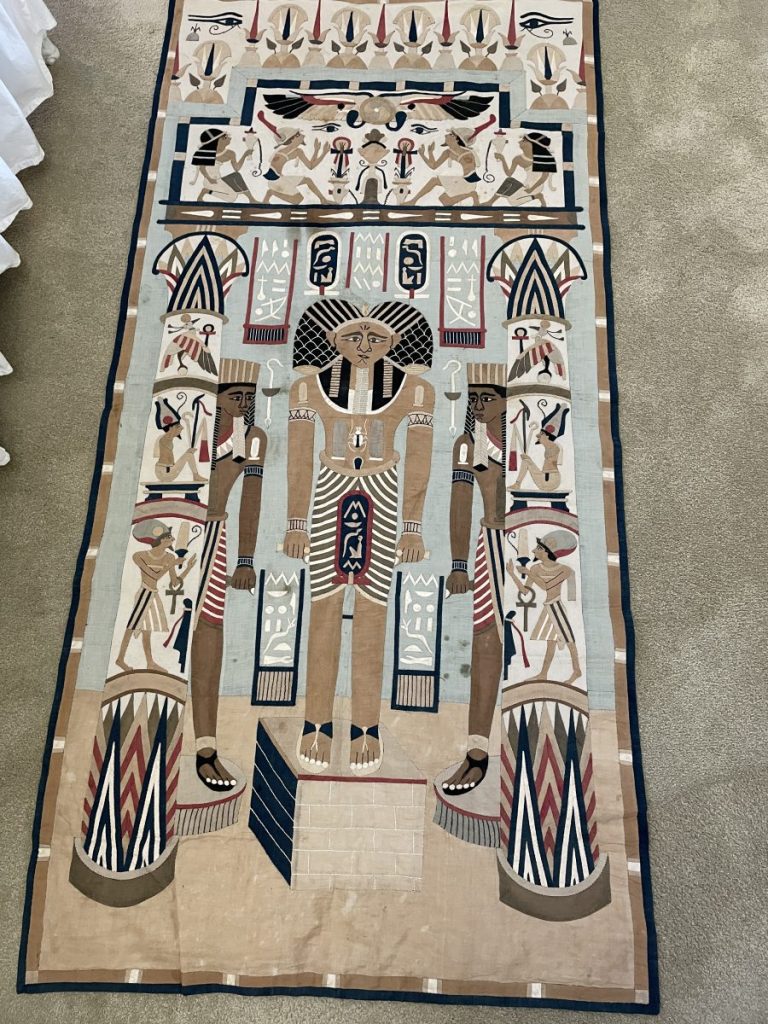 Textile artwork featuring Egyptian motifs, including figures and hieroglyphs in a symmetrical design.