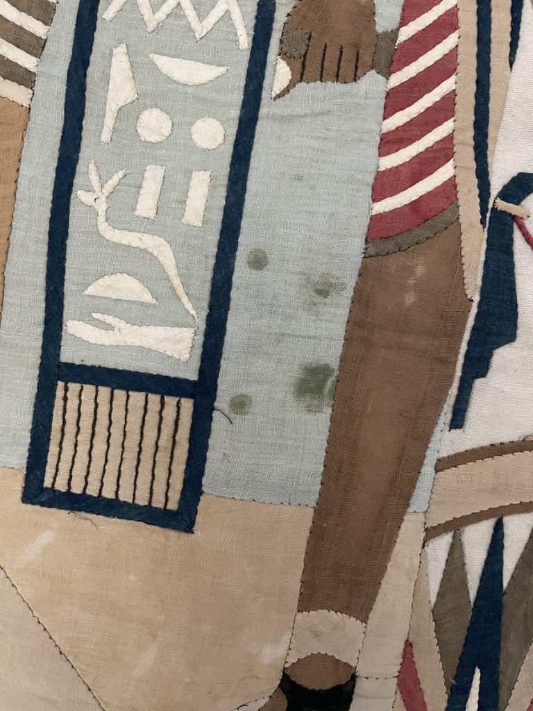 Fragment of an ancient Egyptian textile featuring hieroglyphs and figures in muted colors.