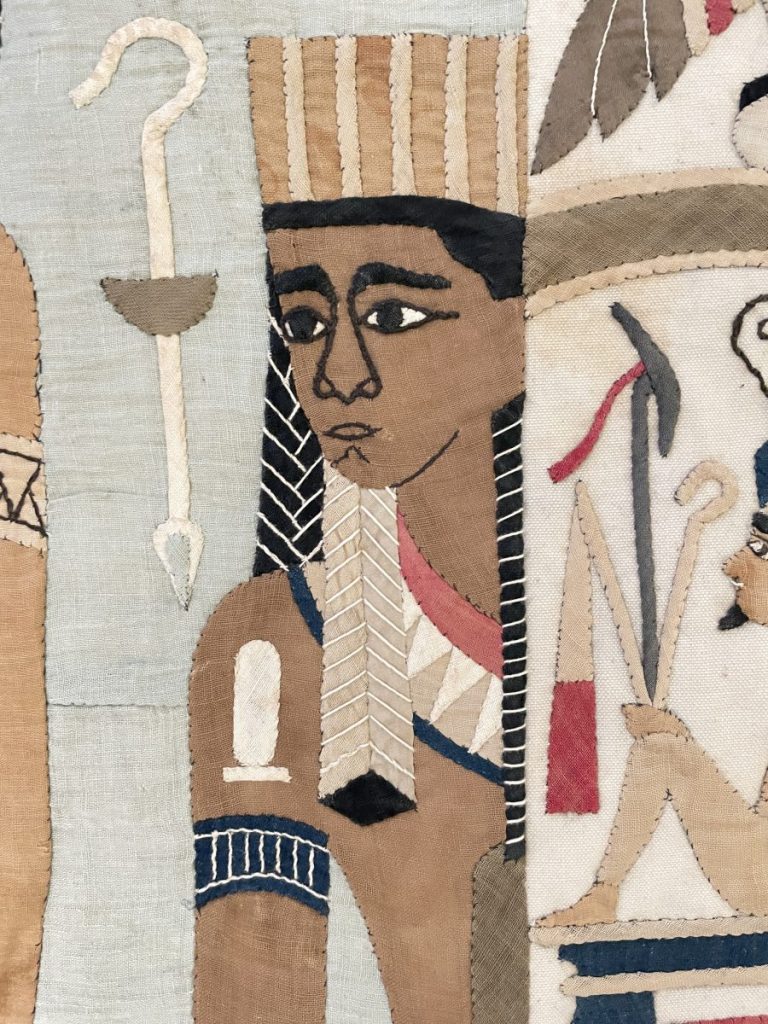 Fragment of an ancient Egyptian textile depicting a figure with a headdress and decorative elements.