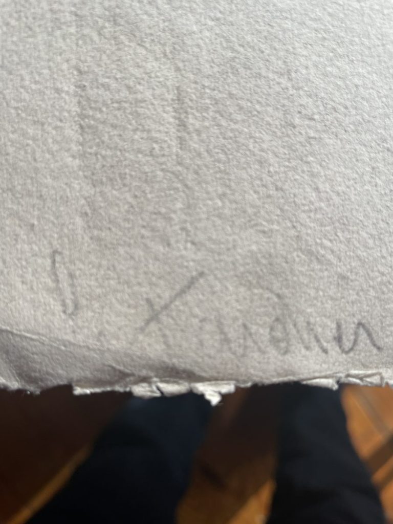 A handwritten signature on a piece of textured paper with visible fibers.