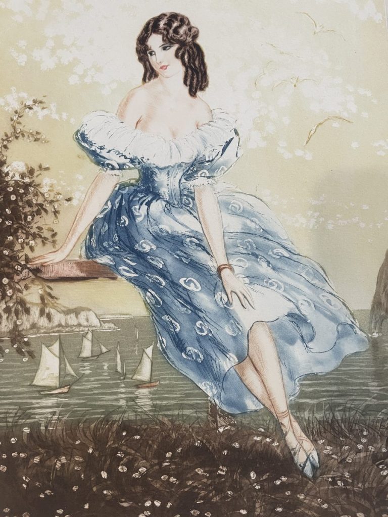 A woman in a blue dress with white patterns sitting near a body of water, surrounded by trees and boats.