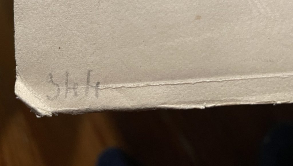 Close-up of a handwritten note that reads 'Shit' on the edge of a piece of paper.
