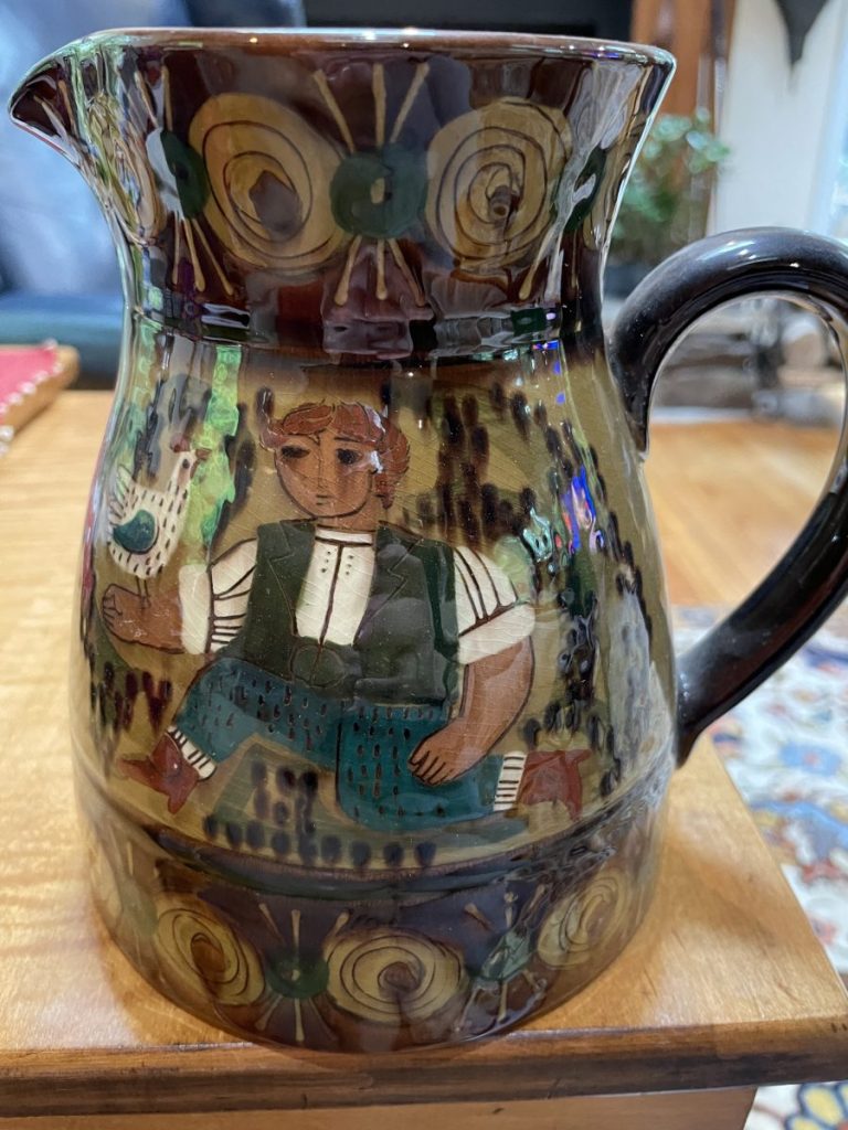 Ceramic pitcher featuring a colorful folk art design with a seated figure and decorative patterns.