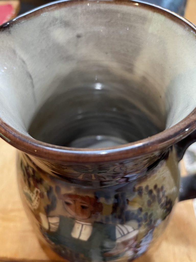 Ceramic pitcher featuring a colorful decorative design on the exterior and a smooth interior.