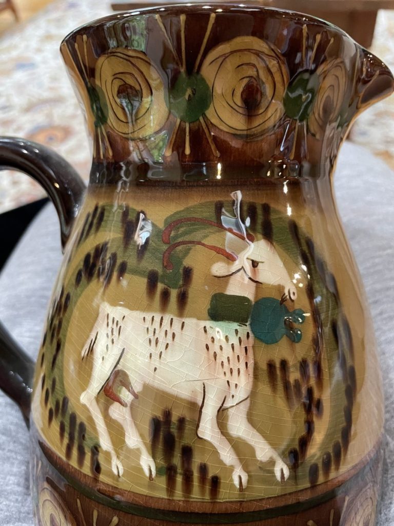 Ceramic pitcher featuring a goat design with decorative patterns in earthy colors.