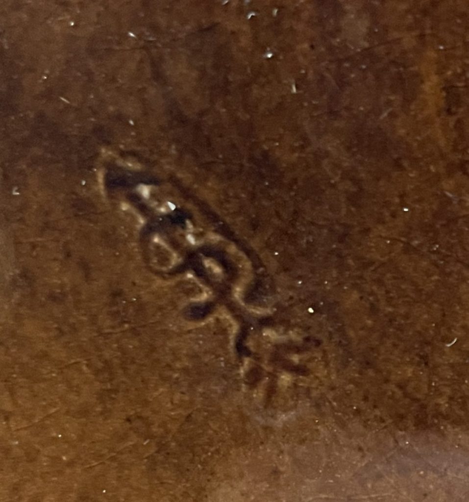 Close-up of an engraved mark on a wooden surface showing a stylized design.
