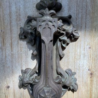 An ornate cast-iron door handle with floral scrollwork stands out against a weathered wooden panel under soft natural light and worn patina.