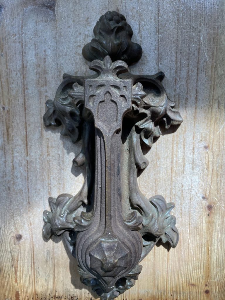 An ornate cast-iron door handle with floral scrollwork stands out against a weathered wooden panel under soft natural light and worn patina.